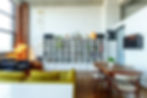 Loft-style living room with a wall of white bookshelves flanked by a brick wall with floor to ceiling windows