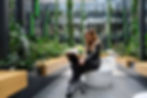 Image of female working on her laptop in an office building lobby embellished with lush greenery suspended from the high ceilings